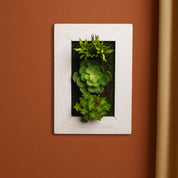 Tiny Frame, vertikales Greendecors Sukkulentenbild im weißen Rahmen an einer warmen Terrakottawand, detailreich bepflanzt mit künstlichen Sukkulenten in satten Grüntönen
