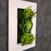 Seitliche Aufnahme eines Tiny Frame mit künstlichen Sukkulenten im weißen Holzrahmen, montiert an einer dunkelgrauen Wand