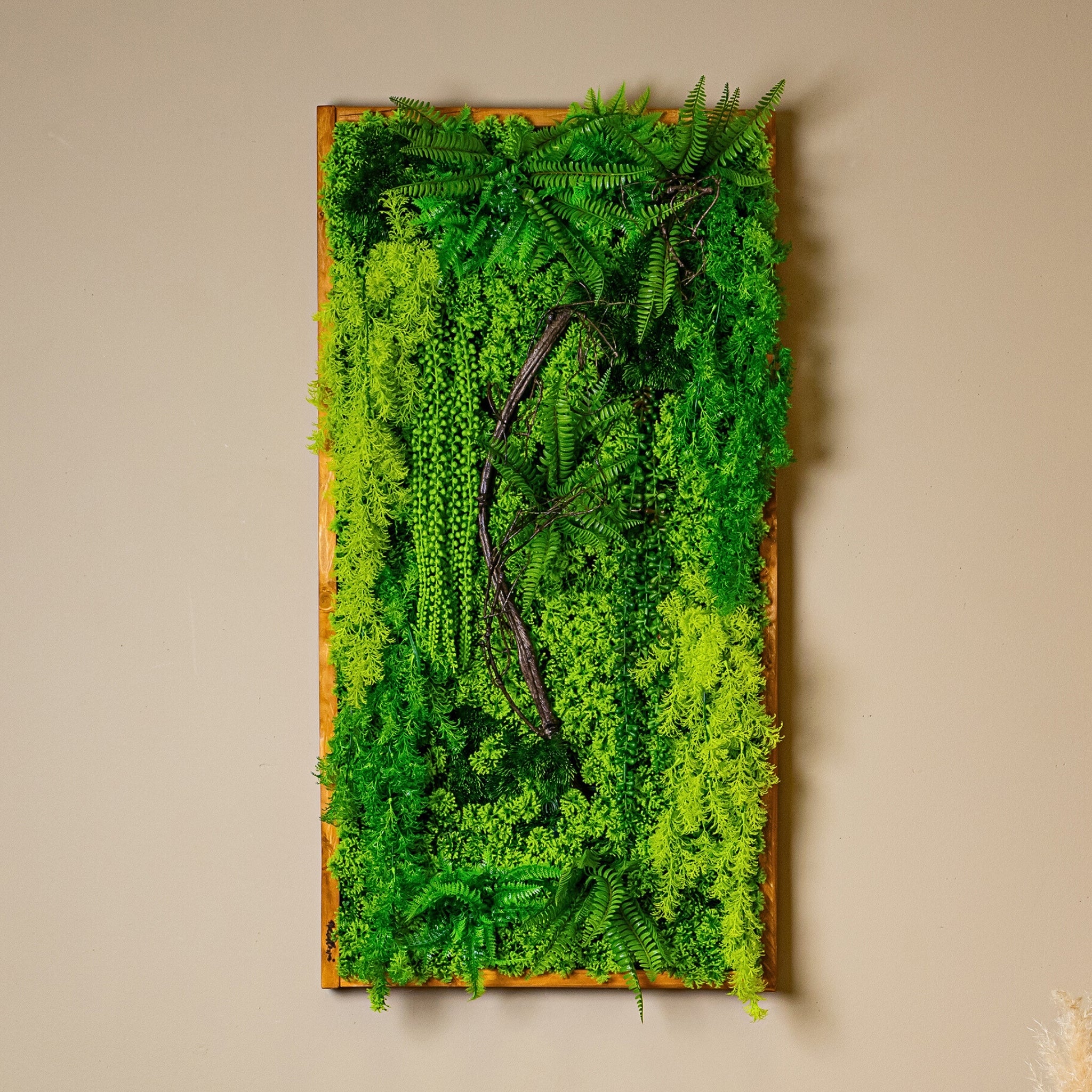 Langformatiges Greendecors Pflanzenbild mit dichten Farnen und künstlichen Ranken an einer beigefarbenen Wand, kombiniert mit Sofa, Tischlampe und modernem Beistelltisch