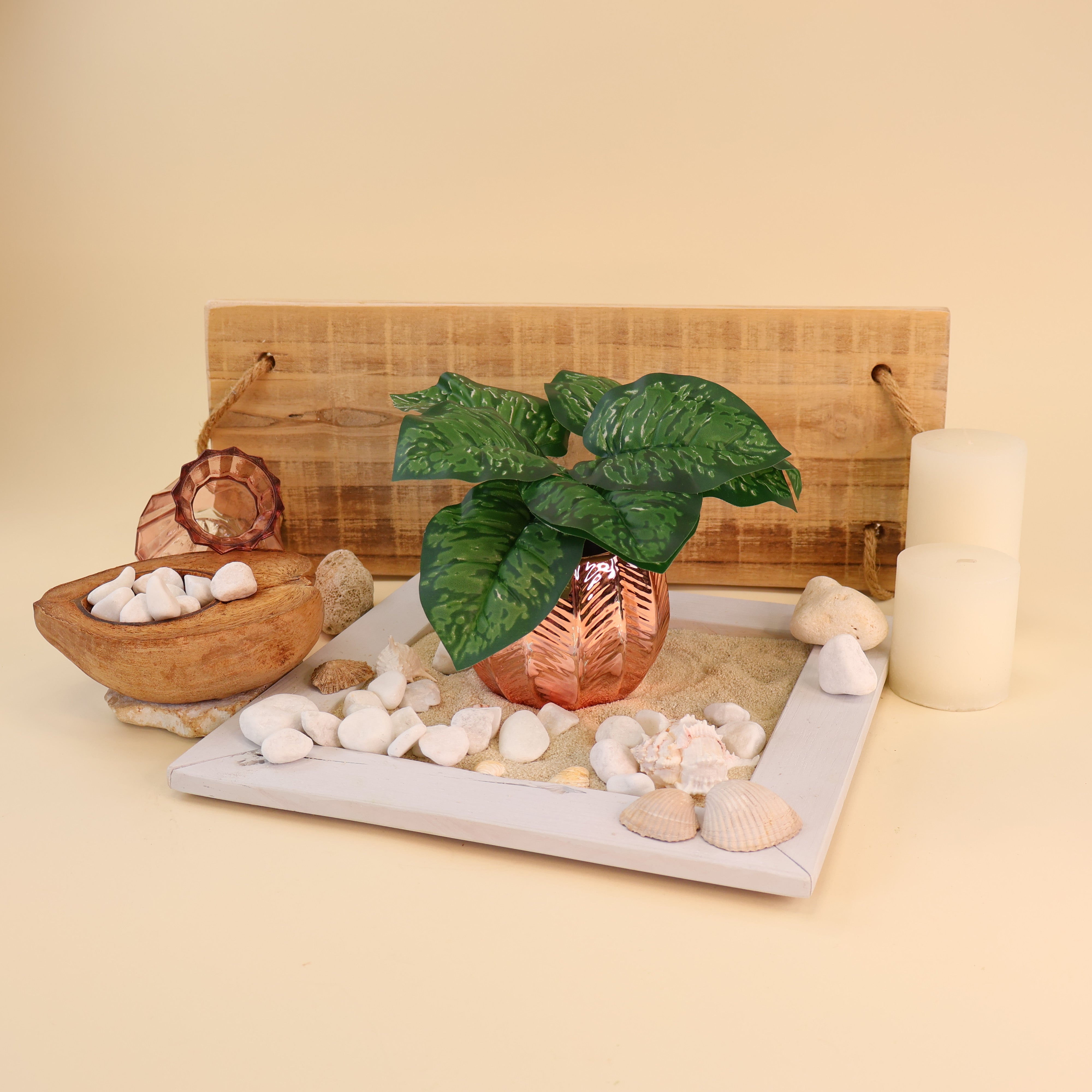 Künstliche Aglaonema mit dunkelgrünen Blättern und hellgrüner Marmorierung dekorativ in einer kupferfarbenen Vase arrangiert. Das Arrangement mit Sand, weißen Kieselsteinen, Muscheln, Kerzen und natürlichen Holzelementen verleiht der Szene eine maritime und moderne Optik. Die detailreiche Blattstruktur und die hochwertige Verarbeitung sorgen für eine realistische Ausstrahlung und machen die Kunstpflanze ideal für Vasen, Regaldekorationen und stilvolle Wohnraumbegrünungen.