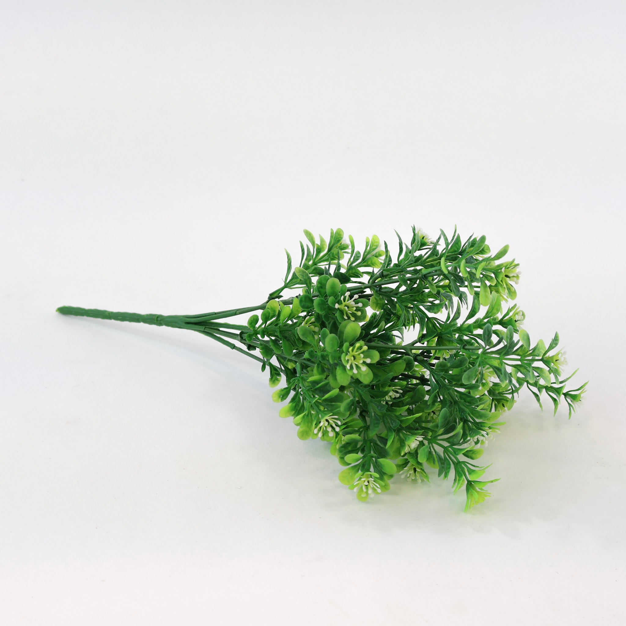 Künstlicher Grünzweig mit kleinen grünen Blättern und feinen weißen Blüten auf weißem Hintergrund, dekorative Kunstpflanze für Wohnraumdeko und Interior-Styling.