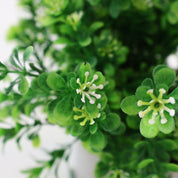 Makroaufnahme eines künstlichen Grünzweigs mit kleinen grünen Blättern und feinen weißen Blüten, detailreiche Kunstpflanze mit natürlicher Optik und unscharfem Hintergrund.