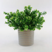 Künstlicher Grünzweig mit kleinen grünen Blättern und feinen weißen Blüten in einem strukturierten Keramiktopf vor weißem Hintergrund, moderne Kunstpflanze für Wohnraumdeko und Shelf Styling.