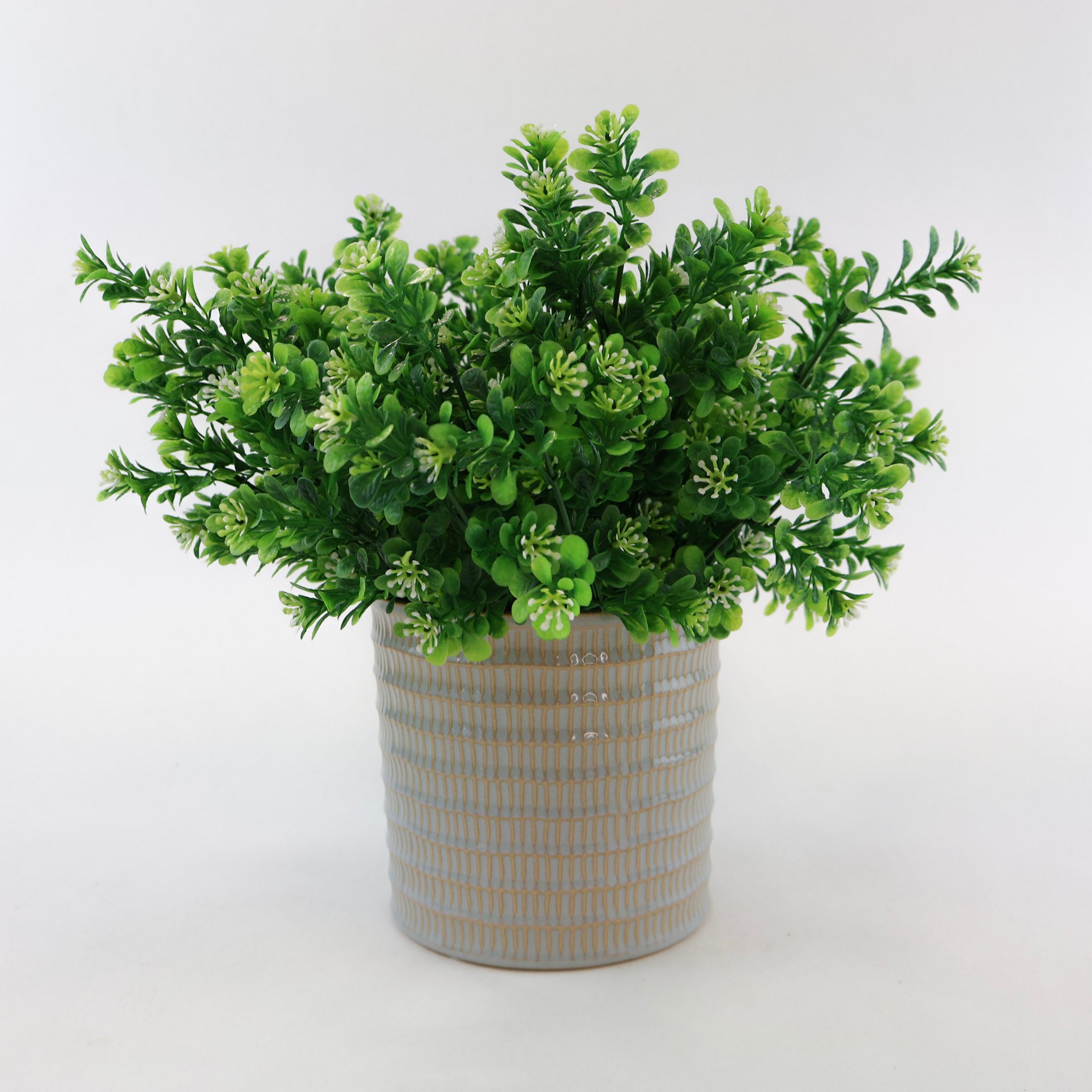 Künstlicher Grünzweig mit kleinen grünen Blättern und feinen weißen Blüten in einem strukturierten Keramiktopf vor weißem Hintergrund, moderne Kunstpflanze für Wohnraumdeko und Shelf Styling.